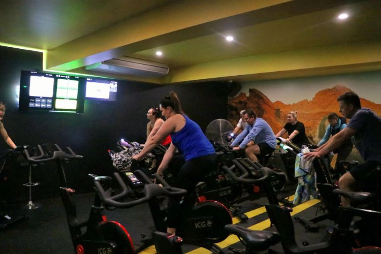 A group of people participating in a spin class, pedalling on stationary bikes at CountryFit