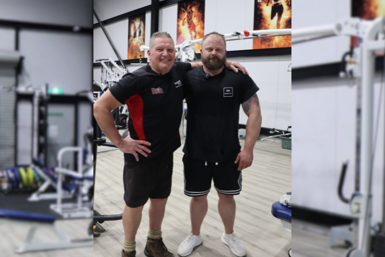 Glenn, the owner of CountryFit Gym Mudgee and Scott stand together in the gym, smiling and posing for the camera. Glenn on the left, wearing a black shirt with red accents and shorts, has a muscular build, while Scott on the right, dressed in a black t-shirt and shorts, showcases his fitness transformation.