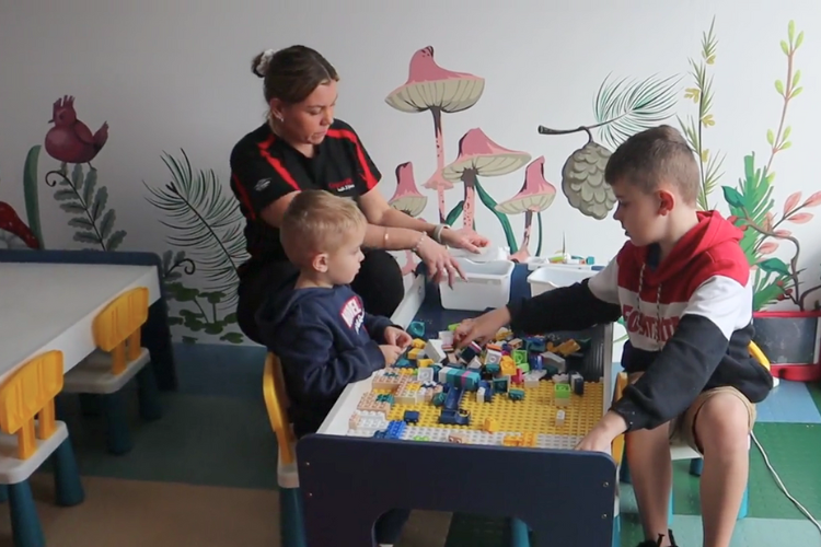 A creche attendant at CountryFit Gym in Mudgee interacts with two children at a colourful activity table filled with building blocks.